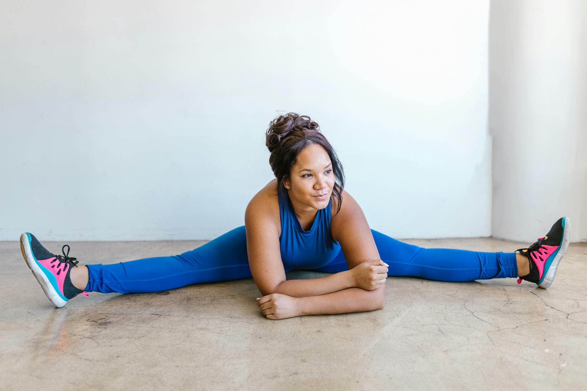 Kobieta plus size w niebieskim stroju ćwiczy rozciąganie bioder na podłodze