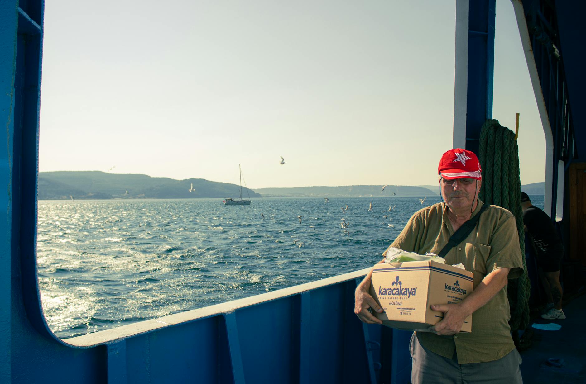 Mężczyzna w czerwonej czapce niesie kartonowe pudło na promie