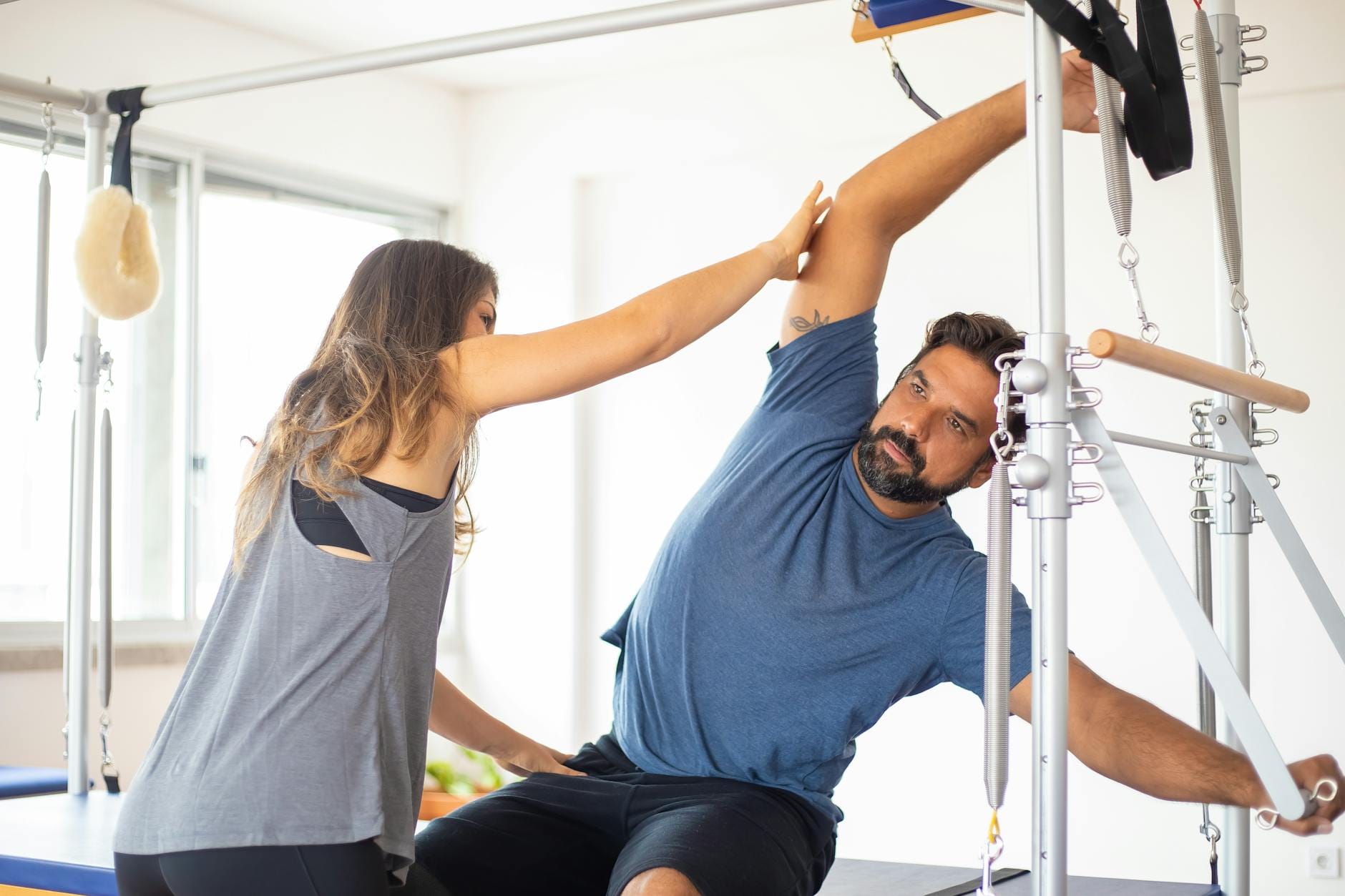 Trener pomaga podopiecznej na reformerze pilates w jasnej siłowni