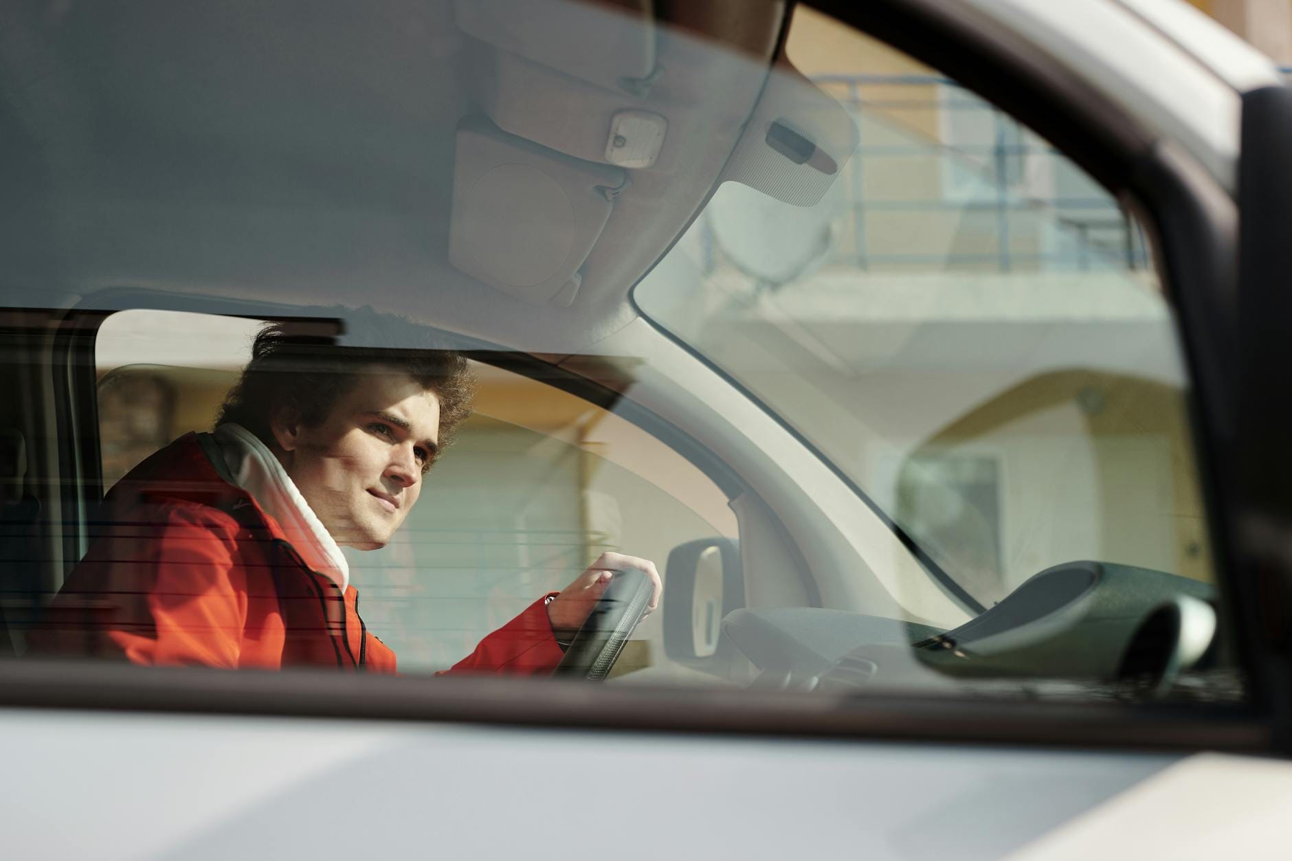 Kierowca w czerwonej kurtce prowadzi auto w słoneczny dzień